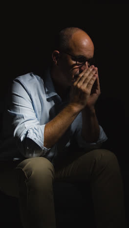 Vertical-Video-Of-Depressed-Mature-Man-Struggling-With-Mental-Health-Sitting-In-Darkness-In-Real-Time-With-Low-Key-Lighting